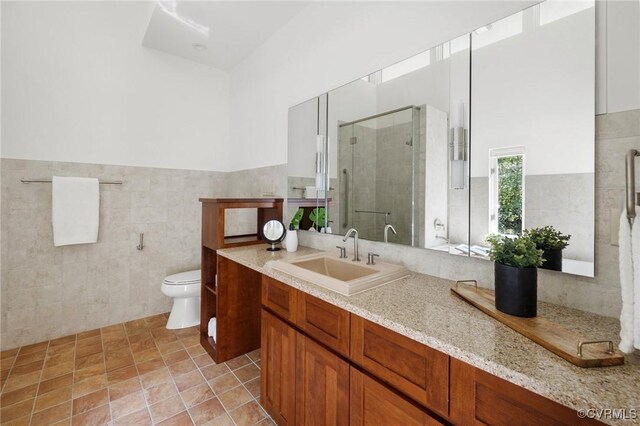 bathroom with tile walls, vanity, toilet, and a shower with door