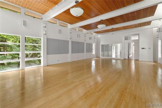 unfurnished living room with light hardwood / wood-style flooring, a high ceiling, and beam ceiling