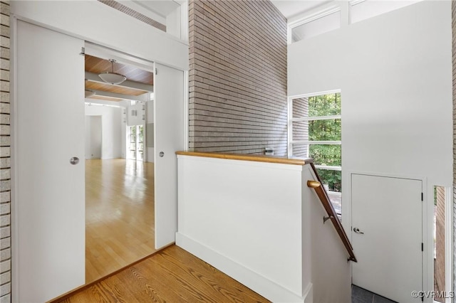 corridor featuring an upstairs landing, beam ceiling, and wood finished floors