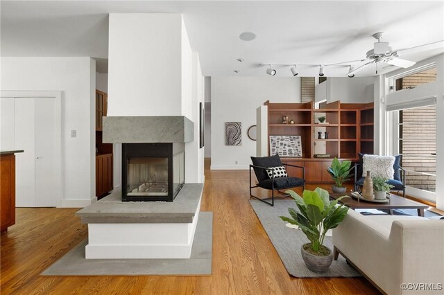 living room featuring ceiling fan, a multi sided fireplace, light hardwood / wood-style flooring, and rail lighting