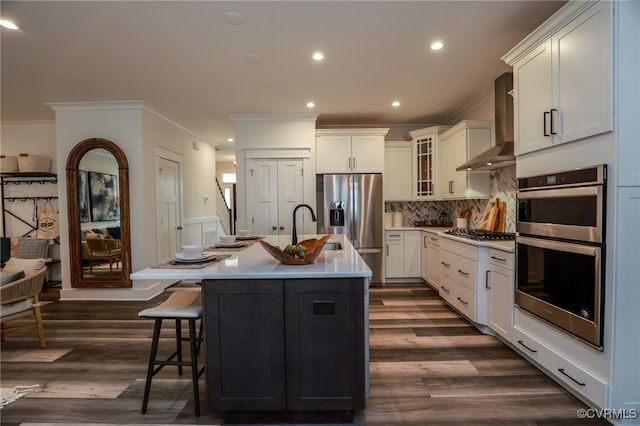 kitchen featuring dark wood-type flooring, wall chimney exhaust hood, a kitchen island with sink, sink, and stainless steel appliances