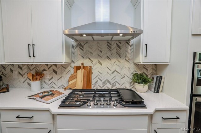 kitchen with wall chimney range hood, decorative backsplash, and white cabinetry