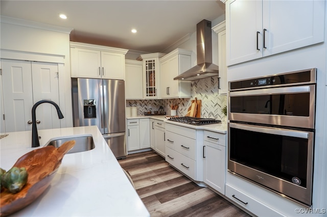 kitchen featuring backsplash, hardwood / wood-style flooring, wall chimney exhaust hood, light stone counters, and stainless steel appliances