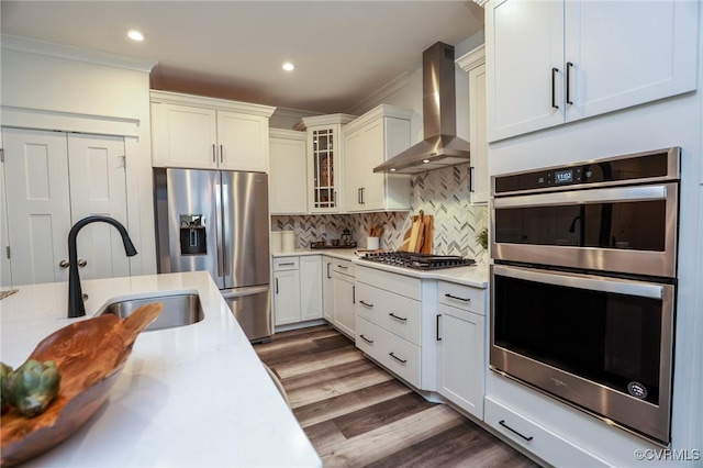 kitchen featuring backsplash, wall chimney range hood, light countertops, stainless steel appliances, and a sink