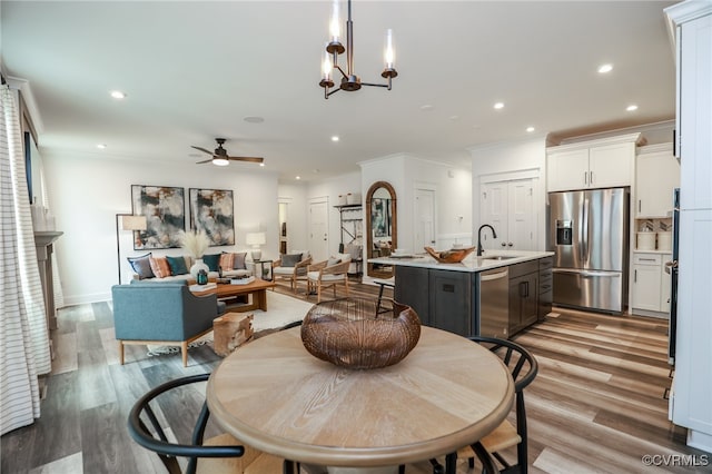 dining room featuring light wood-type flooring, ceiling fan with notable chandelier, sink, and ornamental molding