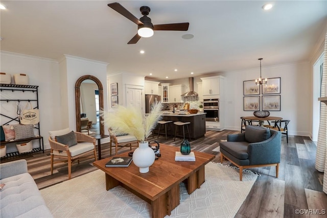 living area featuring wood finished floors, baseboards, arched walkways, crown molding, and ceiling fan with notable chandelier