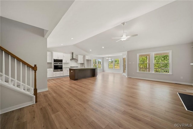 unfurnished living room with stairs, lofted ceiling, light wood-style flooring, ceiling fan with notable chandelier, and a sink