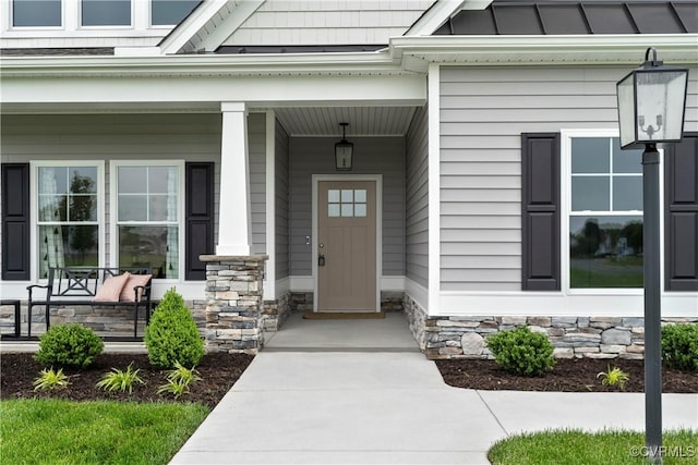 view of exterior entry with stone siding, a porch, and a standing seam roof