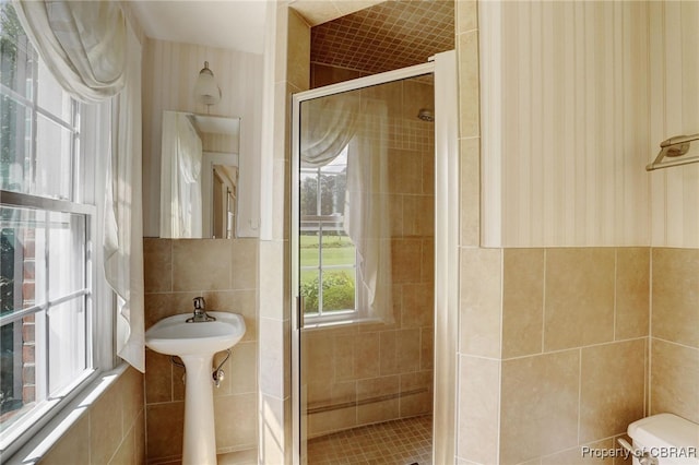 bathroom with tile walls, toilet, and a shower with door