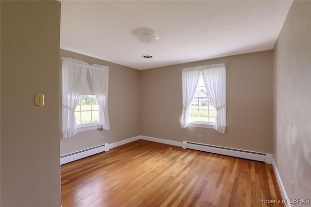 empty room featuring plenty of natural light, baseboard heating, and light hardwood / wood-style flooring