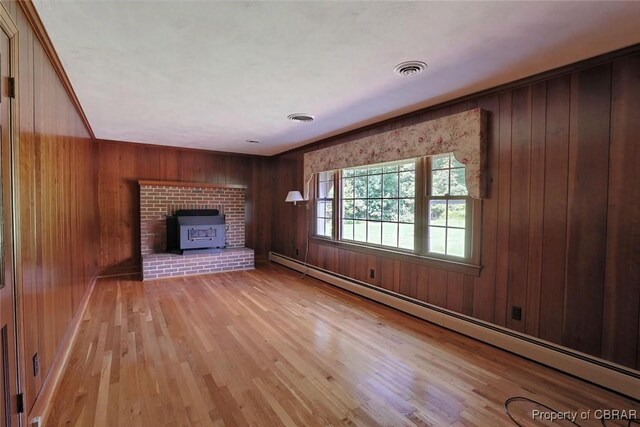 unfurnished living room featuring wood walls, a baseboard radiator, a wood stove, and light wood-type flooring