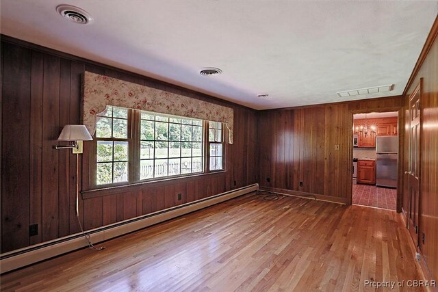 spare room with a notable chandelier, wooden walls, hardwood / wood-style floors, and a baseboard radiator