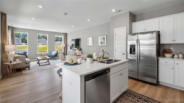 kitchen with light wood finished floors, stainless steel appliances, decorative backsplash, open floor plan, and a sink