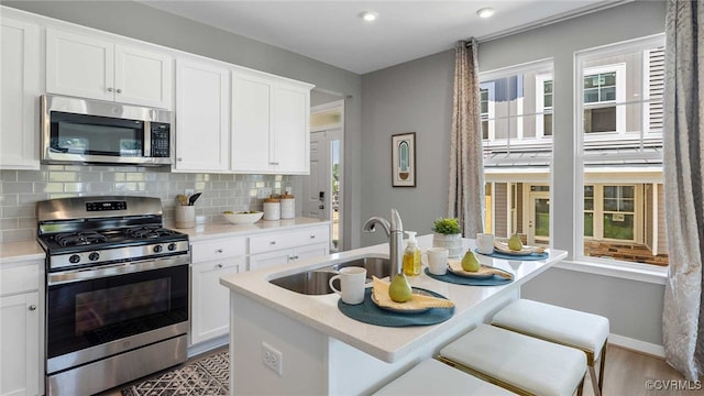 kitchen with stainless steel appliances, a sink, white cabinetry, light countertops, and backsplash