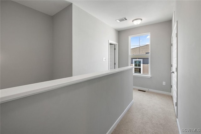 hall with baseboards, visible vents, and light colored carpet