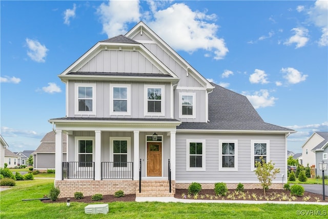 view of front facade featuring covered porch, board and batten siding, a front yard, and roof with shingles