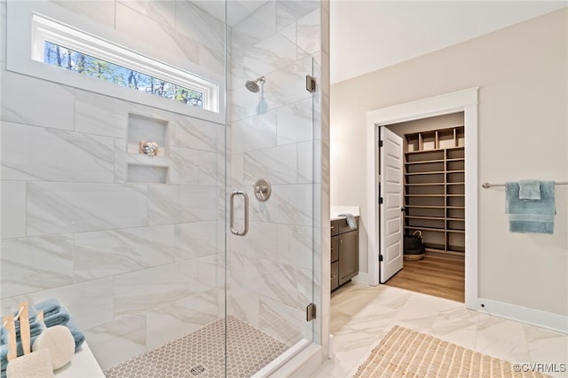 full bath with vanity, a walk in closet, baseboards, and a stall shower