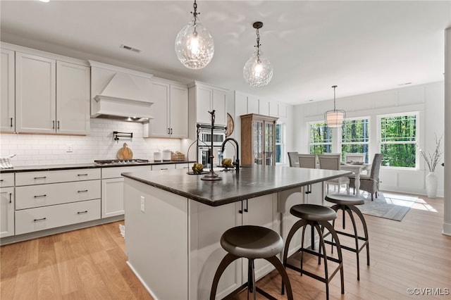 kitchen featuring premium range hood, light wood-type flooring, tasteful backsplash, and dark countertops