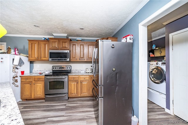 kitchen with stainless steel appliances, wood-type flooring, washer / clothes dryer, and ornamental molding