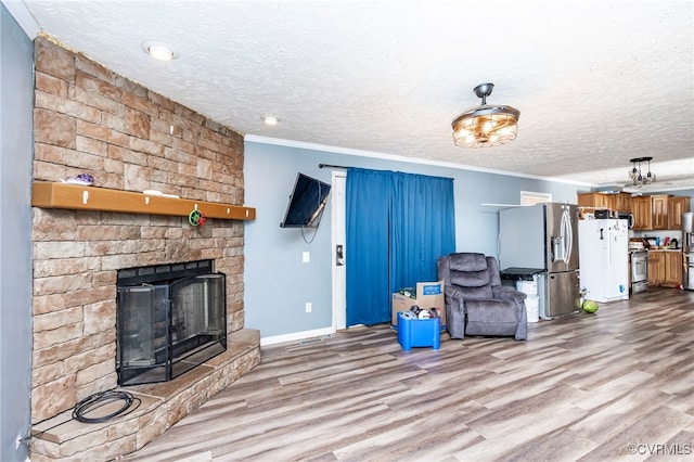 unfurnished living room featuring ornamental molding, light hardwood / wood-style flooring, a textured ceiling, and a stone fireplace