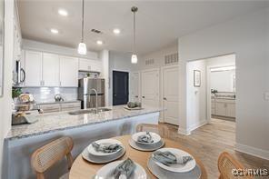 kitchen with sink, decorative light fixtures, light stone counters, white cabinetry, and stainless steel refrigerator