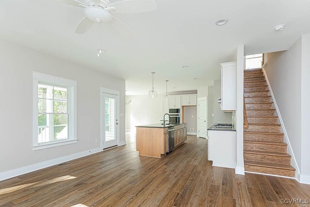 kitchen featuring a kitchen island with sink, dark wood-type flooring, hanging light fixtures, ceiling fan, and white cabinets