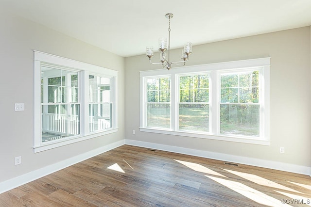 unfurnished dining area featuring hardwood / wood-style floors, a notable chandelier, and a healthy amount of sunlight