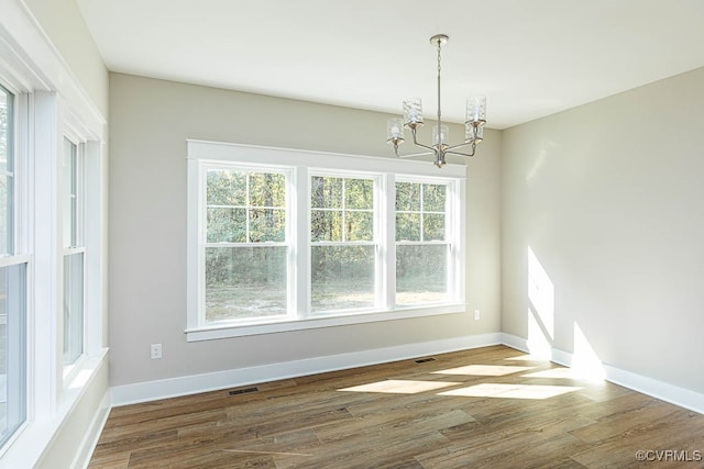 unfurnished dining area with dark wood-type flooring, plenty of natural light, and an inviting chandelier