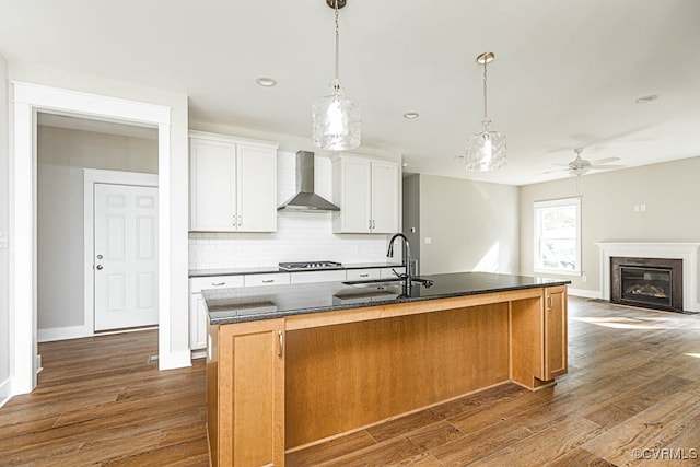 kitchen featuring white cabinetry, ceiling fan, sink, wall chimney exhaust hood, and pendant lighting