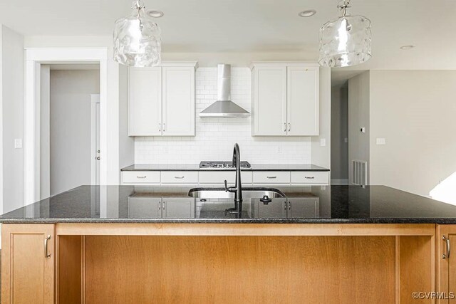 kitchen with an island with sink, wall chimney exhaust hood, and white cabinets