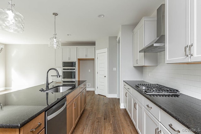 kitchen with dark stone countertops, stainless steel appliances, sink, white cabinets, and wall chimney range hood