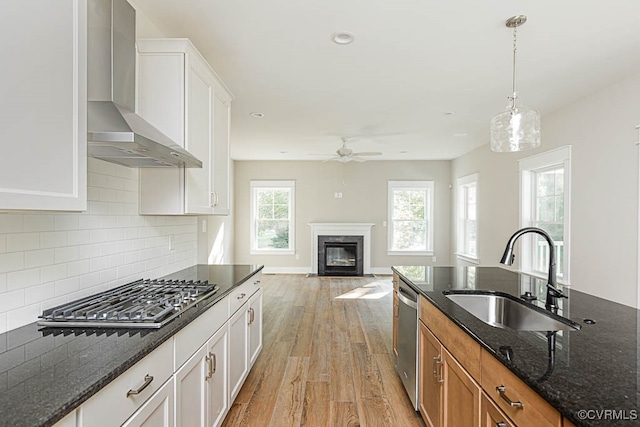 kitchen featuring dark stone countertops, white cabinetry, sink, wall chimney range hood, and a premium fireplace