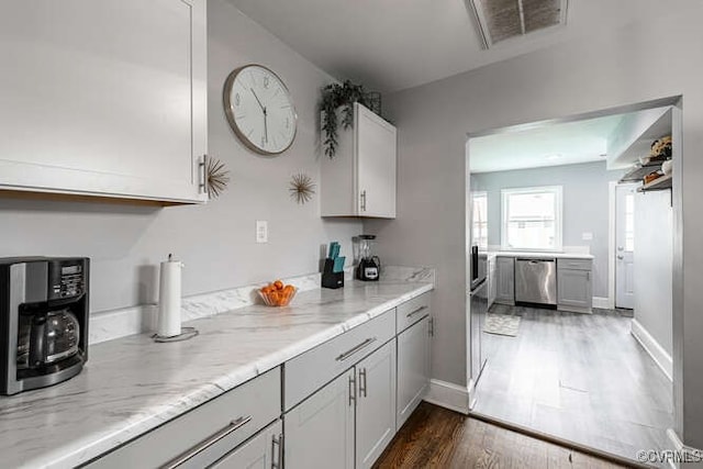 kitchen with light stone countertops, stainless steel dishwasher, white cabinetry, and dark hardwood / wood-style flooring