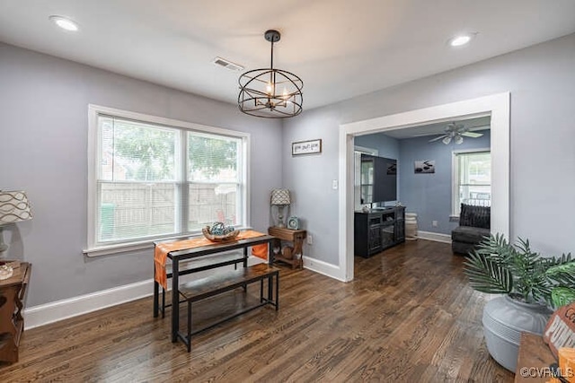 dining space with a healthy amount of sunlight, ceiling fan with notable chandelier, and dark wood-type flooring