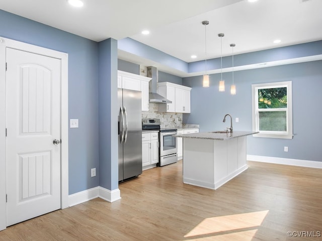 kitchen with wall chimney range hood, white cabinets, stainless steel appliances, and a center island with sink