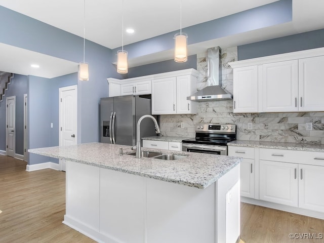 kitchen featuring white cabinets, light hardwood / wood-style flooring, appliances with stainless steel finishes, wall chimney range hood, and a center island with sink