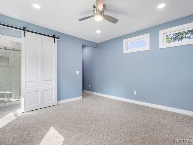 unfurnished bedroom featuring a barn door, ceiling fan, ensuite bathroom, and light colored carpet