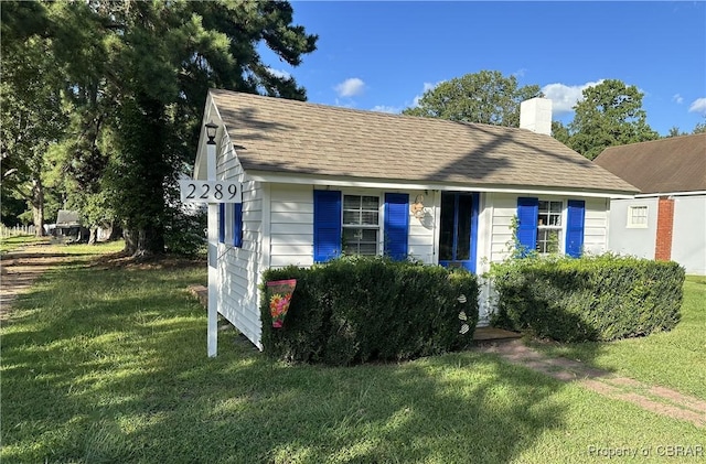 view of front of house with a shingled roof, a front yard, and a chimney