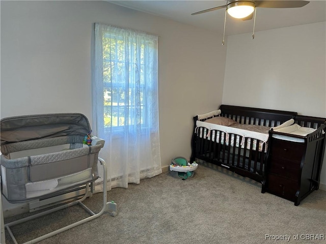 bedroom featuring a nursery area, carpet, and ceiling fan