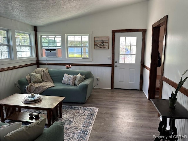 living area with vaulted ceiling, wainscoting, cooling unit, wood finished floors, and a textured ceiling