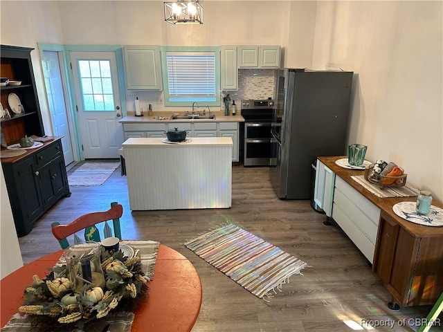 kitchen with wood finished floors, a sink, stainless steel appliances, light countertops, and tasteful backsplash