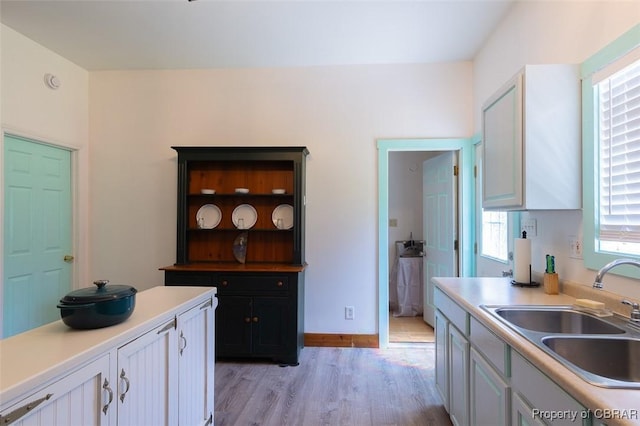 kitchen with light wood finished floors, white cabinetry, light countertops, and a sink