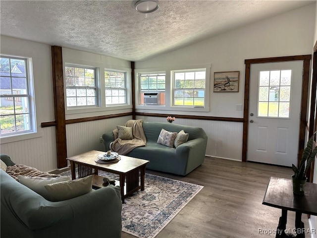 living area with a wainscoted wall, vaulted ceiling, cooling unit, wood finished floors, and a textured ceiling