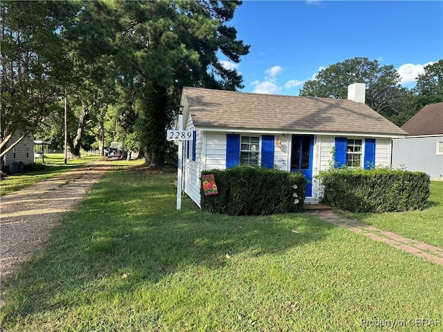 bungalow-style home with a front yard, driveway, roof with shingles, and a chimney