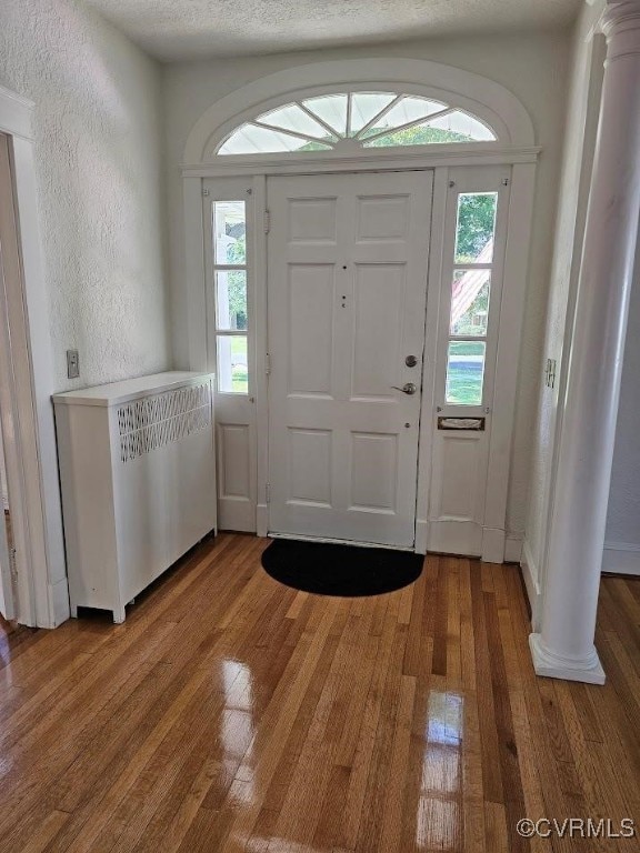 foyer entrance featuring hardwood / wood-style floors, decorative columns, and a wealth of natural light