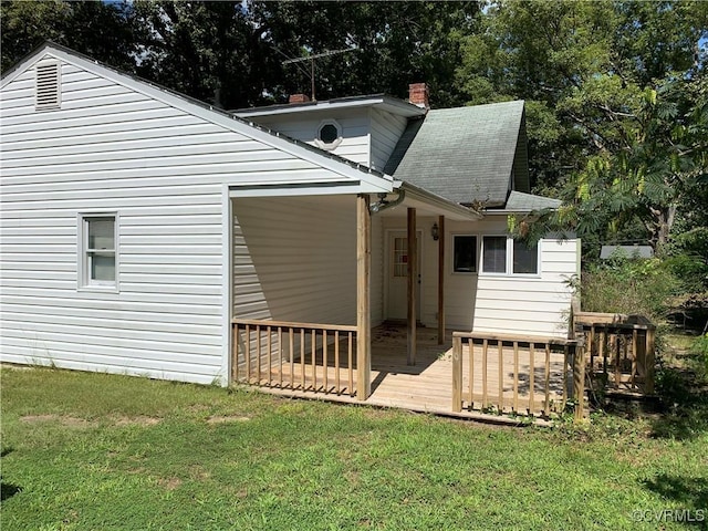 back of property featuring a deck, a lawn, a shingled roof, and a chimney