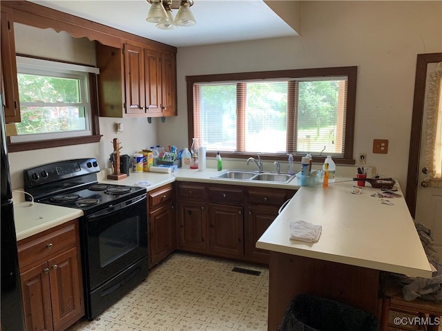 kitchen with a peninsula, a sink, light countertops, black range with electric cooktop, and a wealth of natural light