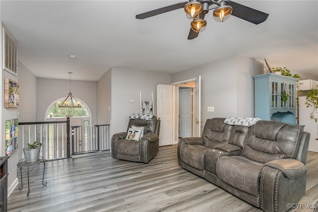 living room with ceiling fan with notable chandelier, light wood-type flooring, and vaulted ceiling