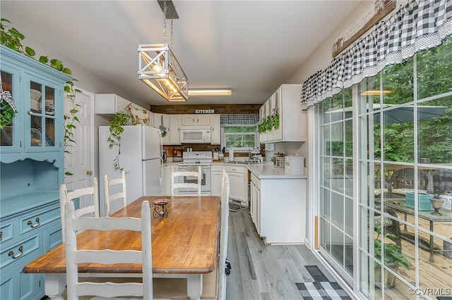 kitchen featuring light wood-type flooring, white appliances, sink, white cabinets, and hanging light fixtures