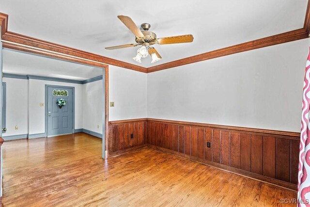 unfurnished room with crown molding, hardwood / wood-style flooring, ceiling fan, and wooden walls